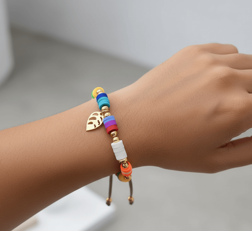 Gold plated charm bracelet featuring colorful beads and a leaf charm on a woman's wrist.