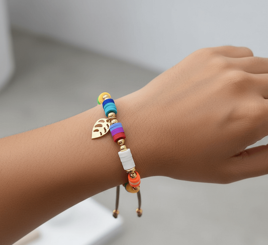 Gold plated charm bracelet featuring colorful beads and a leaf charm on a woman's wrist.