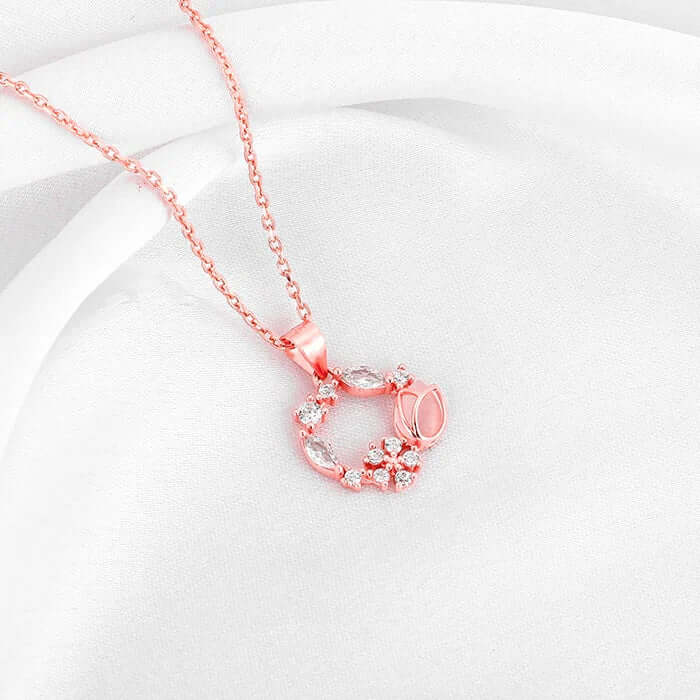 Rose gold necklace featuring floral designs and sparkling accents nestled on soft white fabric.