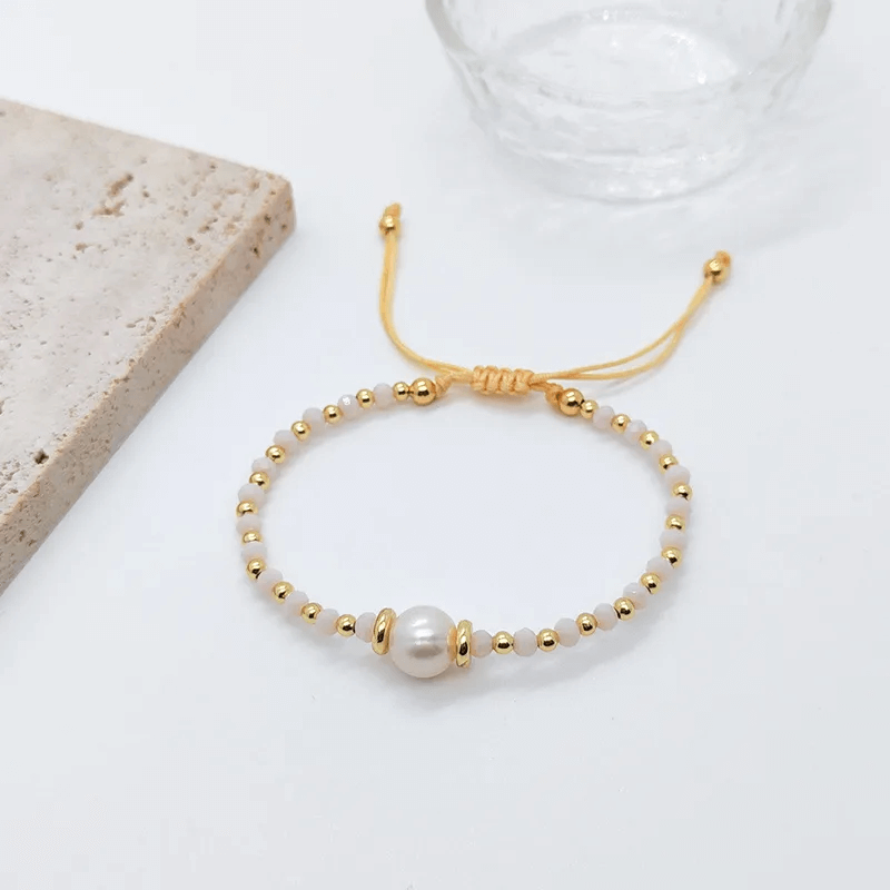 18K gold plated charm bracelet with freshwater pearls on a textured background.