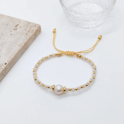 18K gold plated charm bracelet with freshwater pearls on a textured background.