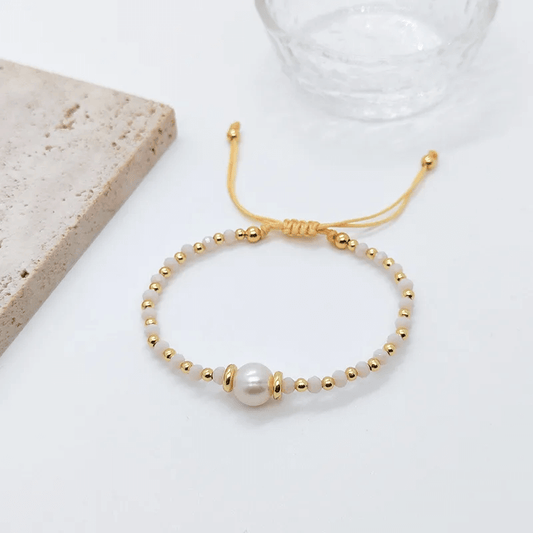 18K gold plated charm bracelet with freshwater pearls on a textured background.