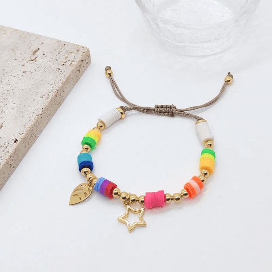 Gold plated charm bracelet with colorful beads and charms on a light background.