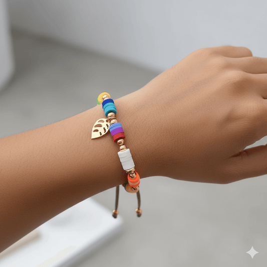 Gold plated charm bracelet featuring colorful beads and a leaf charm on a woman's wrist.